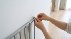 賃貸住宅の壁に突っ張り式ペットゲートを設置する様子。壁紙保護のため、ゴム脚と壁の間に白いウォールセーバーを挟んでいる。日本人女性の手元。