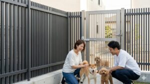 高い縦格子フェンスとオートクローザー付き門扉で脱走対策がされた庭で、柴犬とトイプードルとリラックスする日本人夫婦。