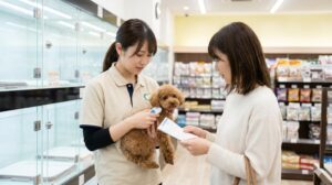 日本のペットショップにて、店員が新しく犬を迎える日本人飼い主に、マイクロチップの装着証明書とスキャン方法について明るい雰囲気で説明している場面。